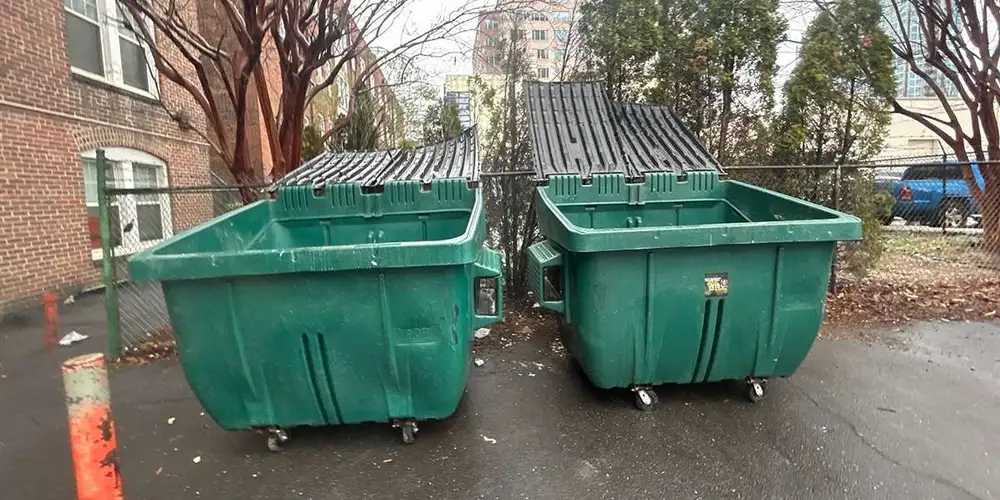 Two green wheeled dumpsters beside a brick building for the Cache, OK dumpster rental guide