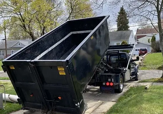 Truck lowering a black roll-off dumpster onto a residential driveway in the Cache rental guide