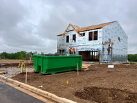 Green construction dumpster beside a house being built in the Elgin, OK rental guide