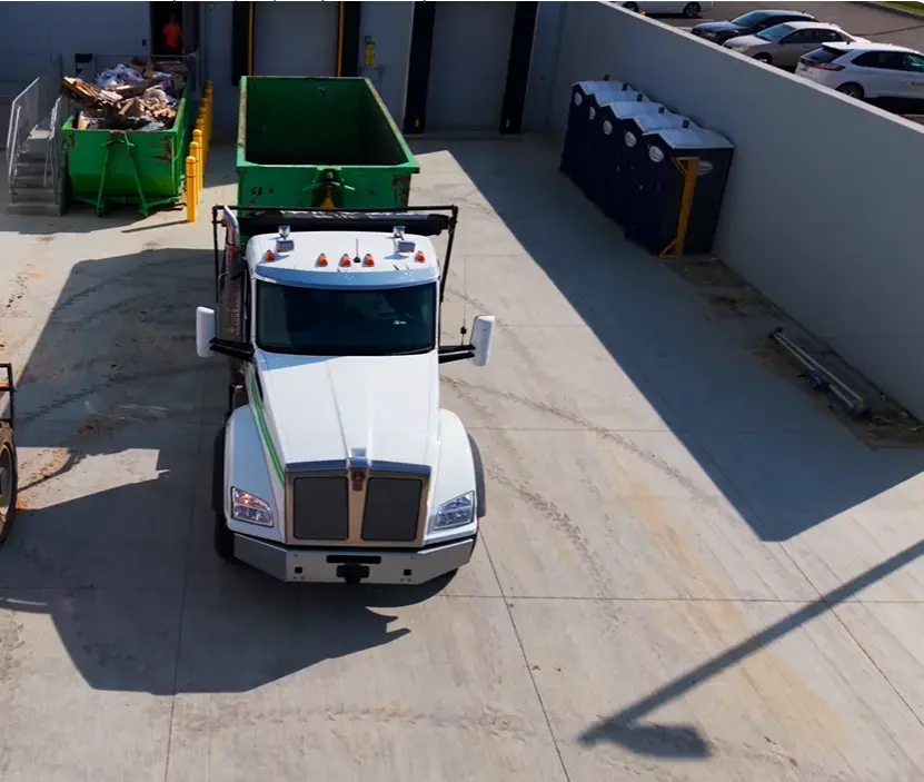 Roll-off truck carrying a green dumpster through a commercial loading area in the Lawton, OK rental guide