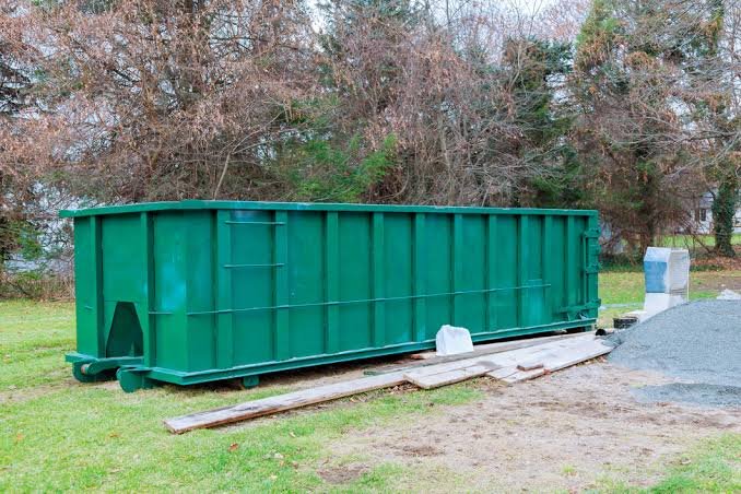 Green roll-off dumpster resting on protective boards beside a driveway