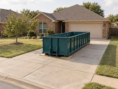 Empty teal roll-off dumpster positioned on a concrete driveway outside a home
