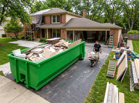 Green roll-off dumpster filled with remodeling debris on a residential driveway