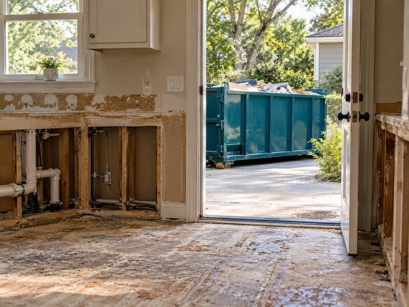 Kitchen renovation with stripped walls and a debris dumpster visible through the doorway