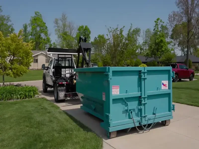 Truck delivering a teal roll-off dumpster to a residential driveway