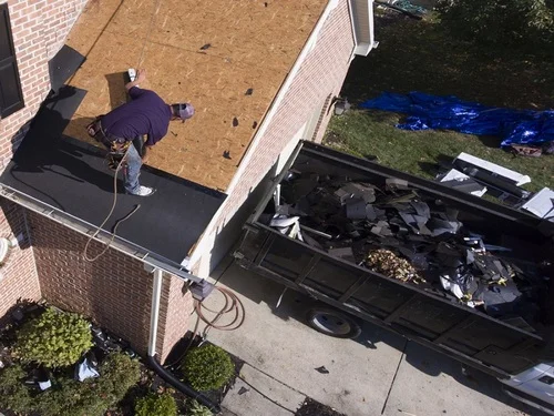 Roofer stripping shingles above a container holding roof tear-off debris