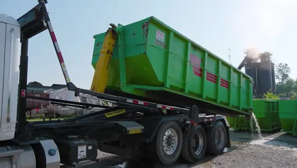 Truck lifting a green roll-off construction dumpster onto its chassis