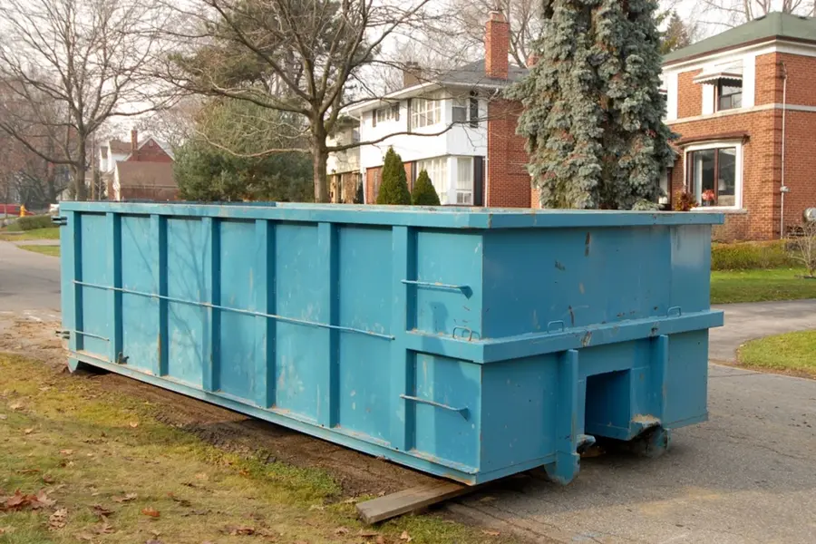 Blue roll-off dumpster beside homes in the Walters, OK property cleanup guide